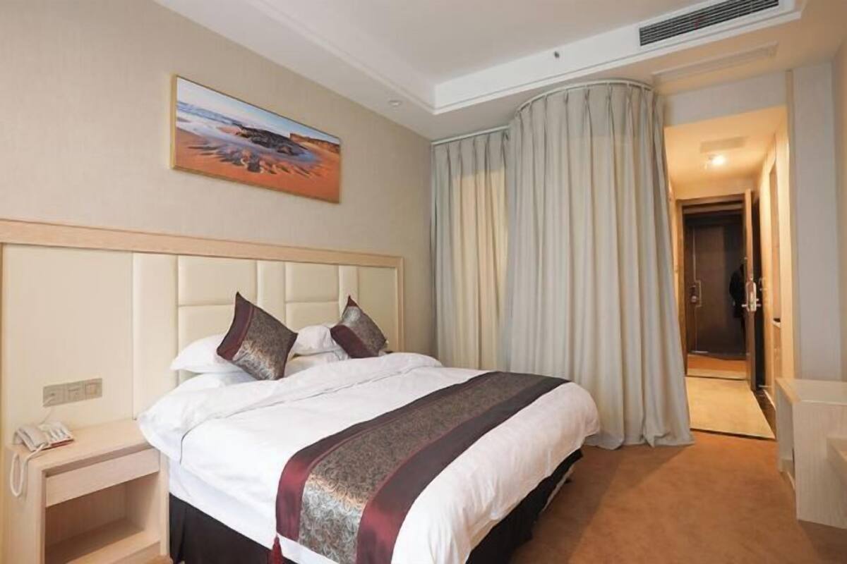 A hotel room with a bed, a painting, a curtain, a nightstand, and a phone.