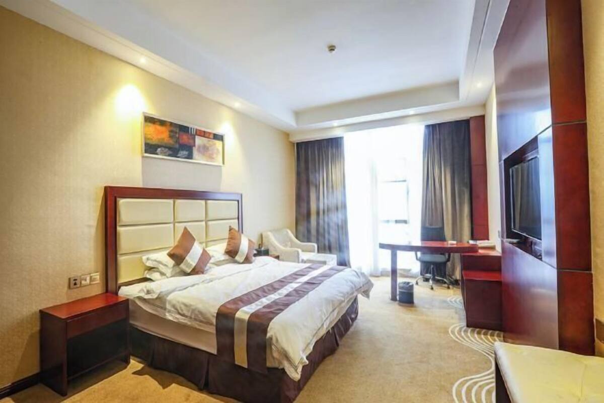 A hotel room with a large bed, a desk, a chair, a television, and a painting on the wall.