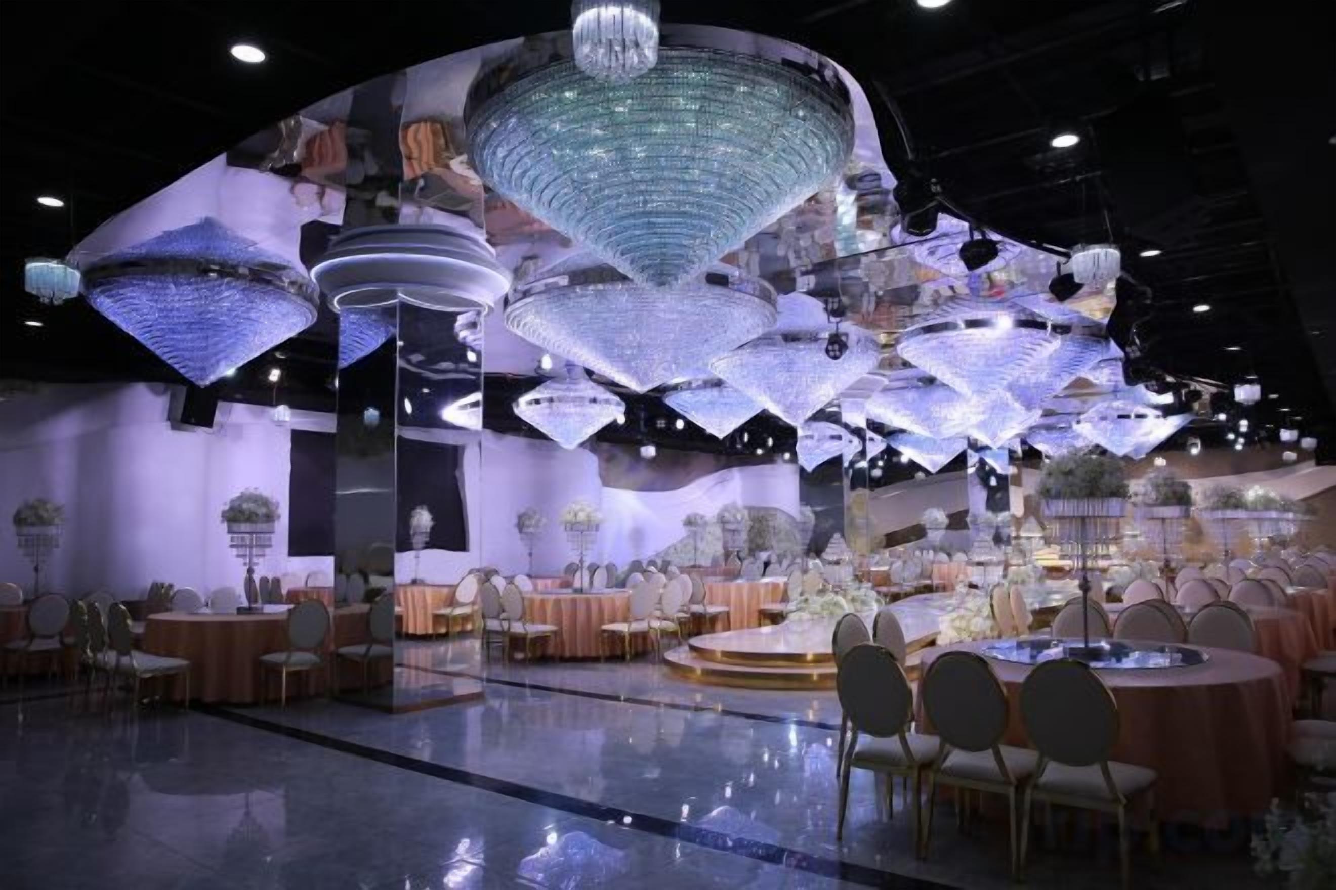 A banquet hall with round tables and chairs, large hanging light fixtures, and a reflective floor.