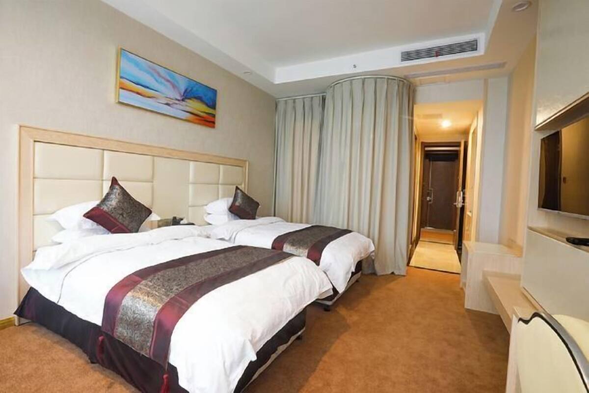 A hotel room with two beds, a large painting on the wall, a television, and a bathroom visible through a doorway.
