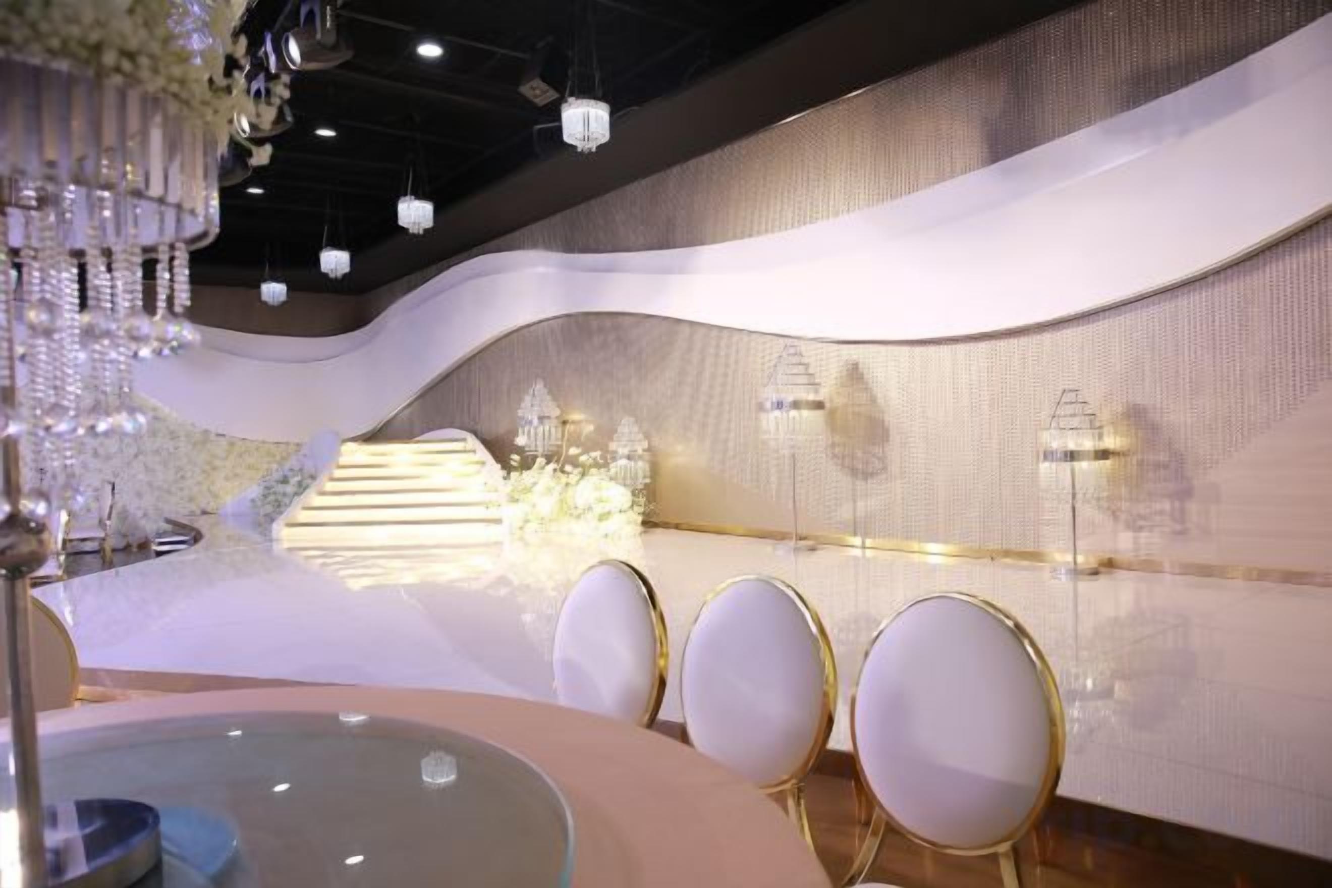 A modern interior with a curved wall, a chandelier, and a seating area with round tables.