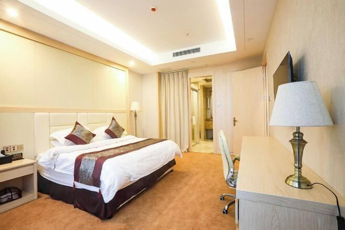 A hotel room with a bed, bedside table, lamp, and a mirror.