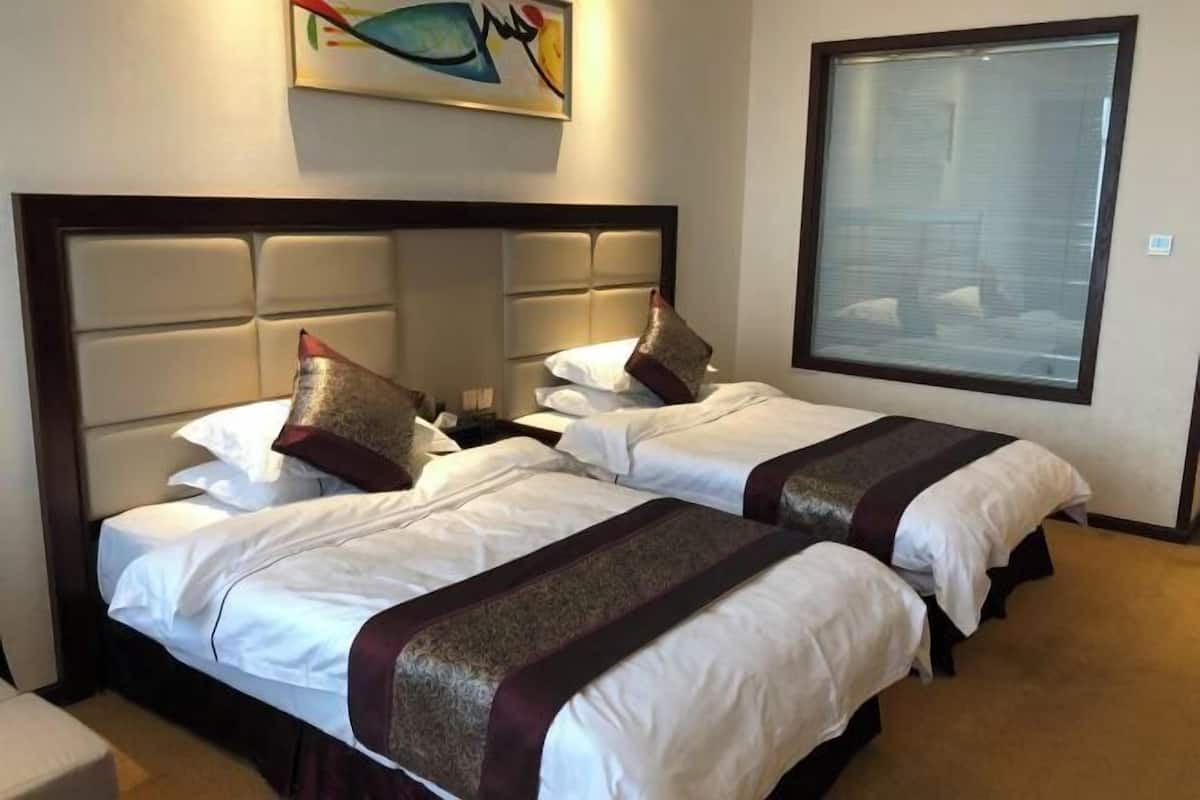A hotel room with two beds, a large window, and a painting on the wall.