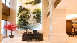 Un hall d’entrée avec un comptoir de réception, trois chaises, une plante en pot et une grande fresque murale représentant un paysage naturel.