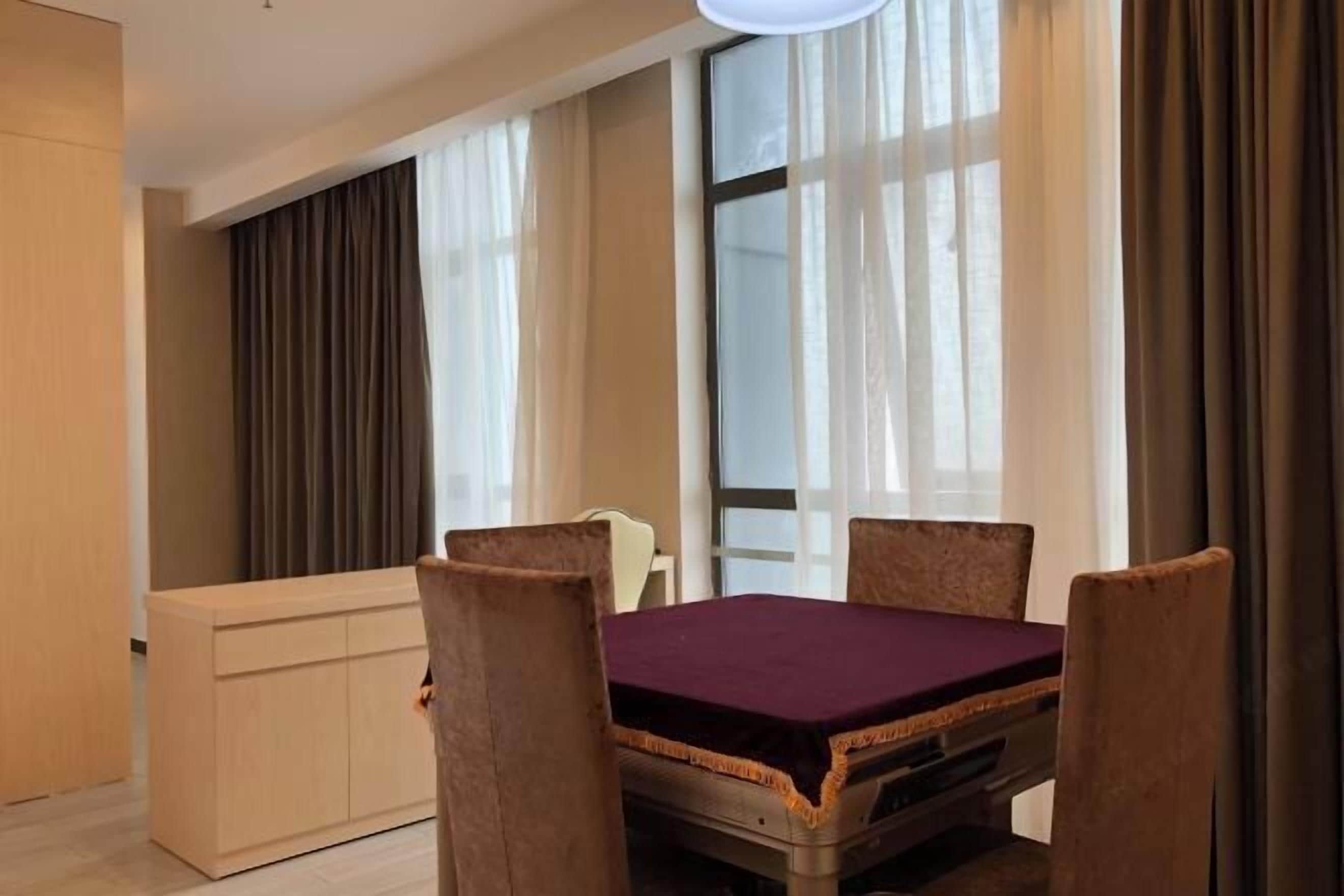 A hotel room with a dining table, four chairs, a sofa, and a large window with curtains.