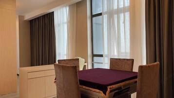 A hotel room with a dining table, four chairs, a sofa, and a large window with curtains.