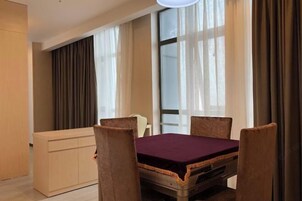 Habitación de hotel con una mesa de comedor, cuatro sillas, un sofá y un ventanal con cortinas.