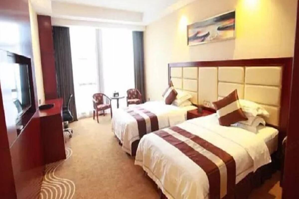 A hotel room with two beds, a TV, a desk, and a window.