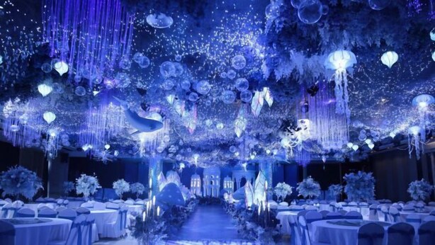 Une salle de banquet avec des tables rondes et des chaises, une allée centrale et des décorations suspendues.