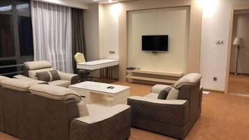 A modern hotel room with a sofa set, a coffee table, a TV mounted on the wall, and a desk with a chair.