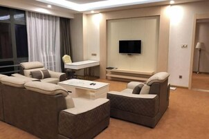 Una habitación de hotel moderna con un conjunto de sofá, una mesa de centro, un televisor montado en la pared y un escritorio con una silla.