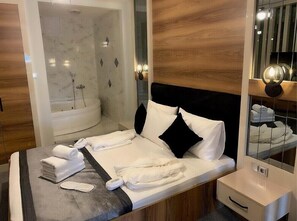 A modern hotel room with a large bed, a separate shower area, and a vanity with a mirror. - OTEL374 (Bolu)