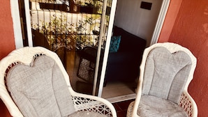 Two wicker chairs with grey cushions placed on a tiled floor, next to a glass door leading outside. - acogedor apartamento acceso directo al jardín en primera linea zona con segurida (La Guáyiga)