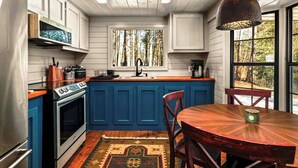 Eine moderne Küche mit blauen Schränken, einem Holztisch und einem großen Fenster mit Blick auf einen Wald.