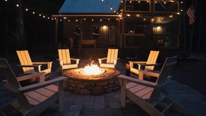 Ein Steinkamin wird von Holz-Adirondack-Stühlen umgeben, darüber hängen Lichterketten.