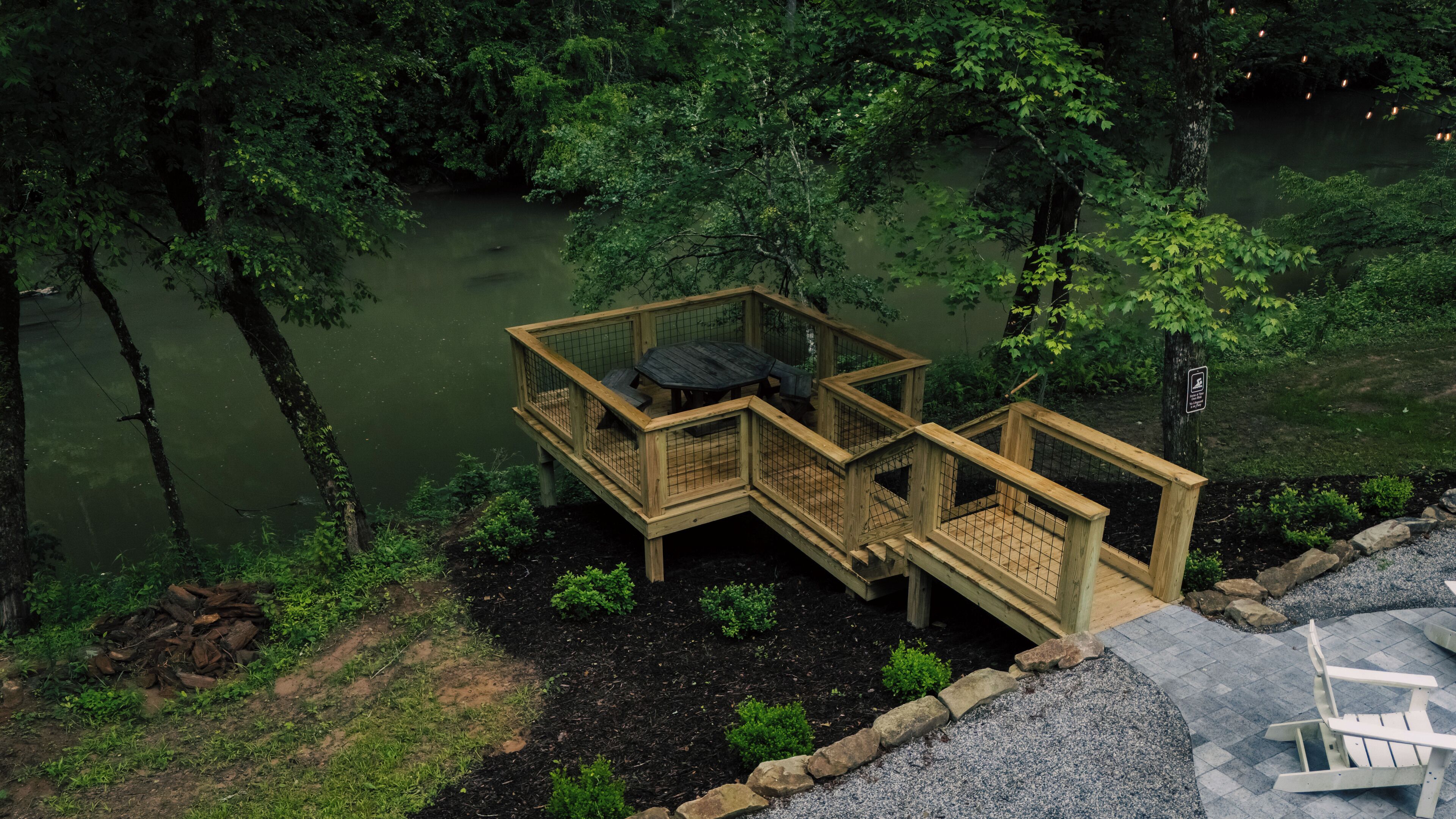 A wooden deck with a table and chairs overlooking a body of water, surrounded by dense greenery.