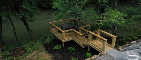 A wooden deck with a table and chairs overlooking a body of water, surrounded by dense greenery.