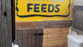 Une salle de bain avec un panneau jaune sur lequel on peut lire « RANCH-WAY Feeds » et des toilettes blanches.