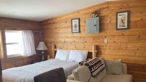 A wooden cabin room with a bed, a sofa, a small table, and two framed pictures on the wall. - Couple get away retreat in Red Feather Lakes!! (Red Feather Lakes)