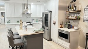 Una cucina moderna con mobili bianchi, elettrodomestici in acciaio inossidabile, un'isola centrale con sgabelli da bar e un angolo dedicato al caffè.