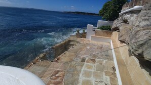 Una escalera de piedra lleva a una terraza con vistas al mar, con un muro rocoso y una vista del litoral.