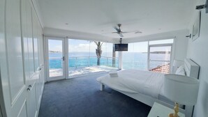 Un dormitorio con cama, ventilador de techo, televisión y vista al mar.