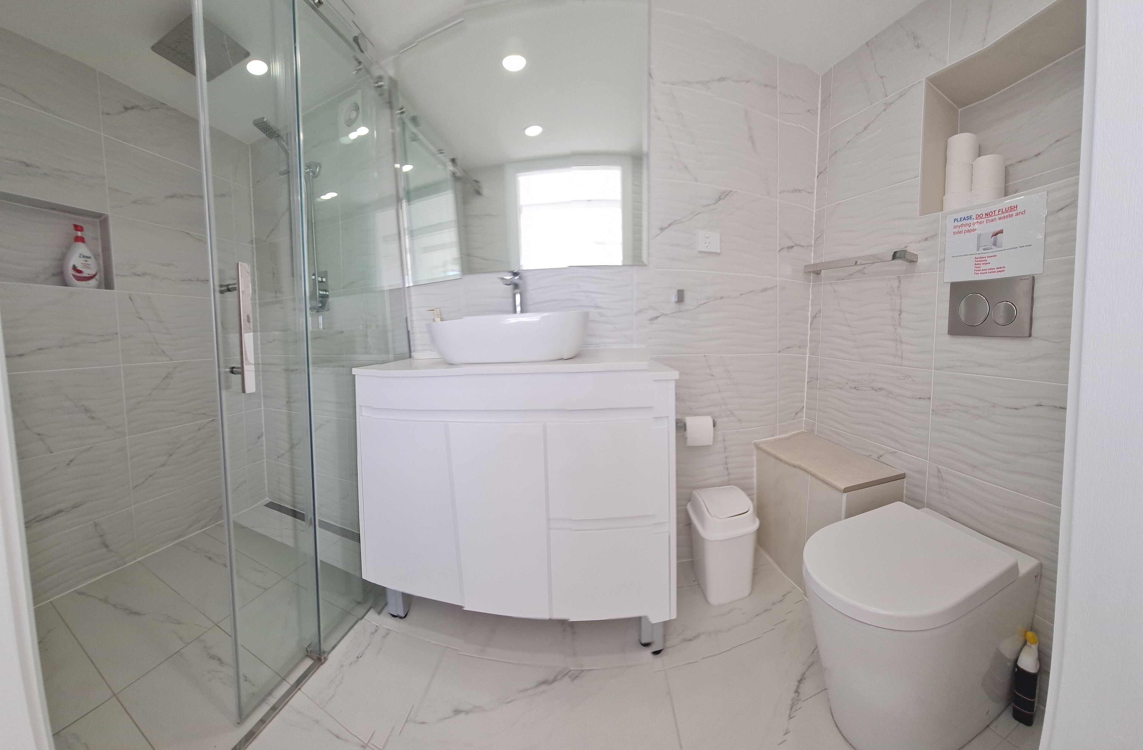 A modern bathroom with a glass-enclosed shower, a white sink, and a toilet.