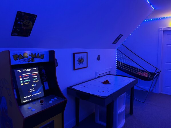 Una habitación con una mesa de hockey sobre hielo, una máquina arcade de Pac-Man y una hamaca.