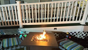 Eine Terrasse mit Feuerstelle, bequemen Sitzgelegenheiten und einem weißen Zaun.