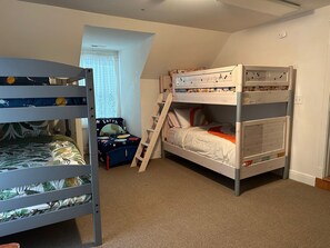 Habitación con literas, una escalera, una ventana con persianas y un escritorio pequeño con una silla.