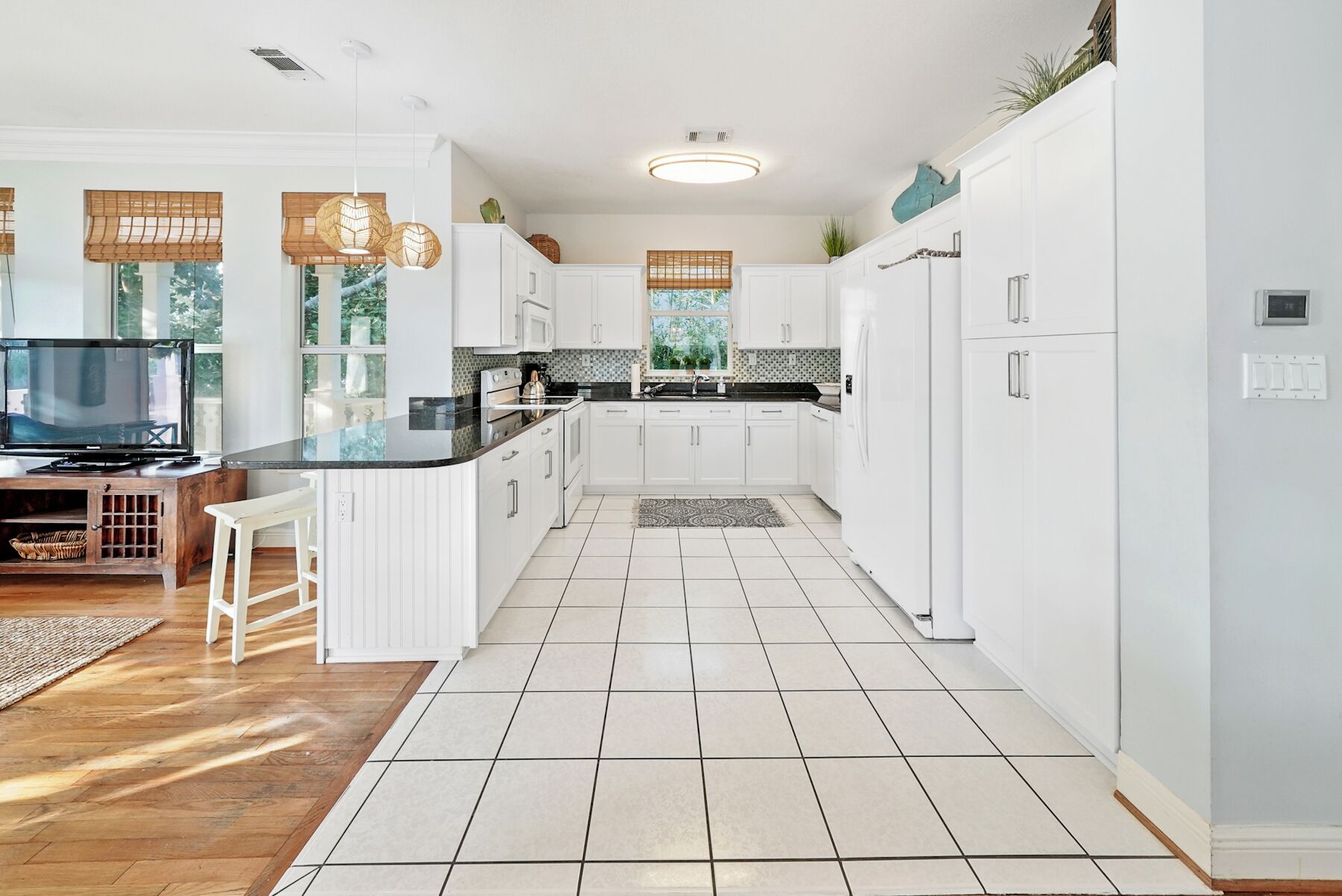 A modern kitchen with white cabinetry, a black countertop, and a tiled floor.