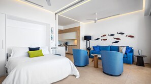 A modern hotel room with a bed, a blue sofa, a coffee table, and a dining area in the background.