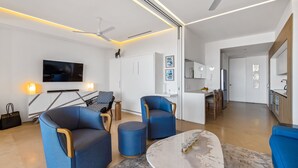 Ein modernes Wohnzimmer mit Flachbildfernseher, zwei blauen Sesseln, einem Couchtisch und einem Essbereich mit Küche im Hintergrund.