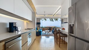 Eine moderne Küche mit Blick ins Freie, ausgestattet mit Edelstahlgeräten, einer Kaffeemaschine und einem Essbereich mit blauen Sitzgelegenheiten.