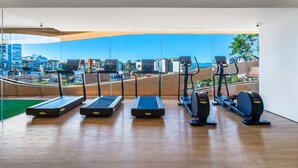 Ein Fitnessstudio mit Laufbändern und Crosstrainern, große Fenster mit Blick auf die Stadt.