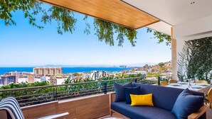 Ein Balkon mit einer Couch, Stühlen und einem Tisch, mit Blick auf die Stadt und das Meer.