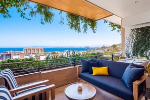 Ein Balkon mit einer Couch, Stühlen und einem Tisch, mit Blick auf die Stadt und das Meer.