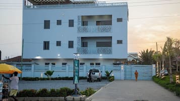 Un edificio moderno con fachada plana, varios balcones y una entrada protegida por una reja.