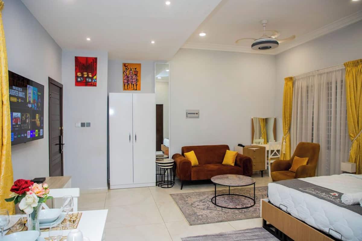 A hotel room with a bed, a sofa, a coffee table, a TV, and a dining area with a table and chairs.