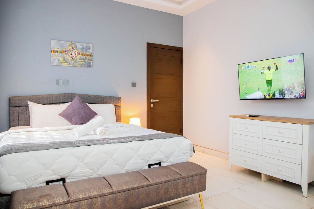Une chambre à coucher comprenant un lit, un banc, un téléviseur, une porte et une œuvre d’art accrochée au mur.
