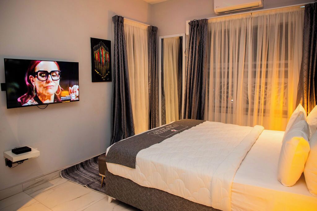 Ett hotellrum med en säng, en tv på väggen och gardiner.