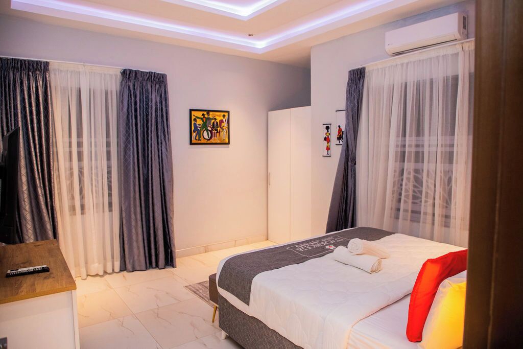 Quarto de hotel com cama, cortinas, ar condicionado e uma obra de arte na parede.