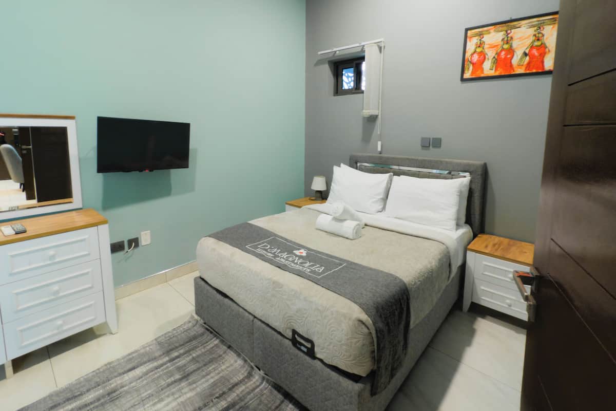 A bedroom with a bed, a TV, a desk, and a small window.