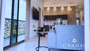 A modern living room with a grey sofa, a small round table, and a TV mounted on the wall. - D'Magnolia Luxury Apartments (Madina)