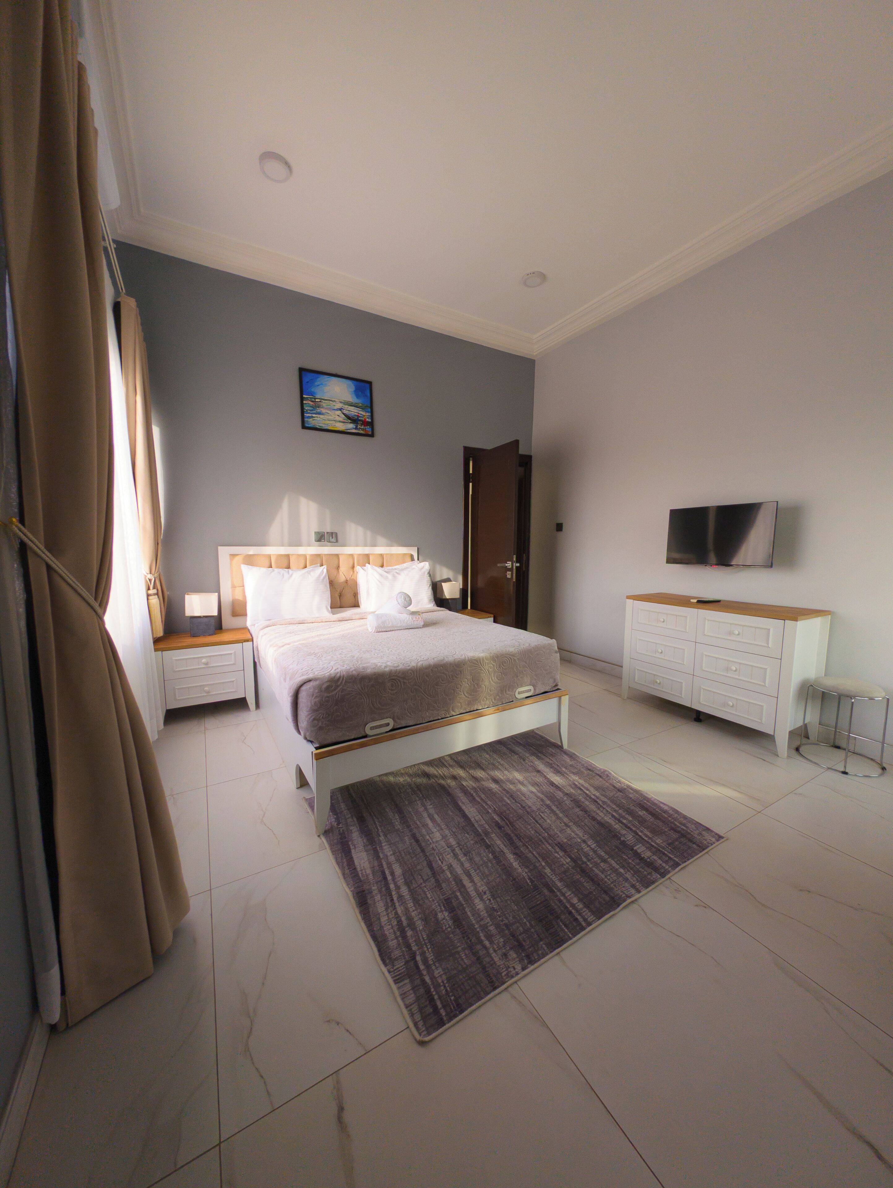 A modern bedroom with a bed, bedside tables, a TV, and a painting on the wall.