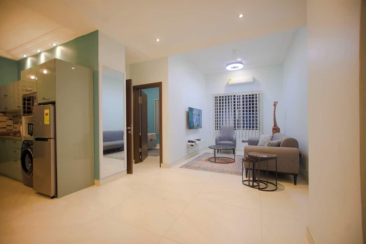 A modern apartment with a kitchen, a living area with a sofa and a coffee table, and a hallway leading to a bedroom.