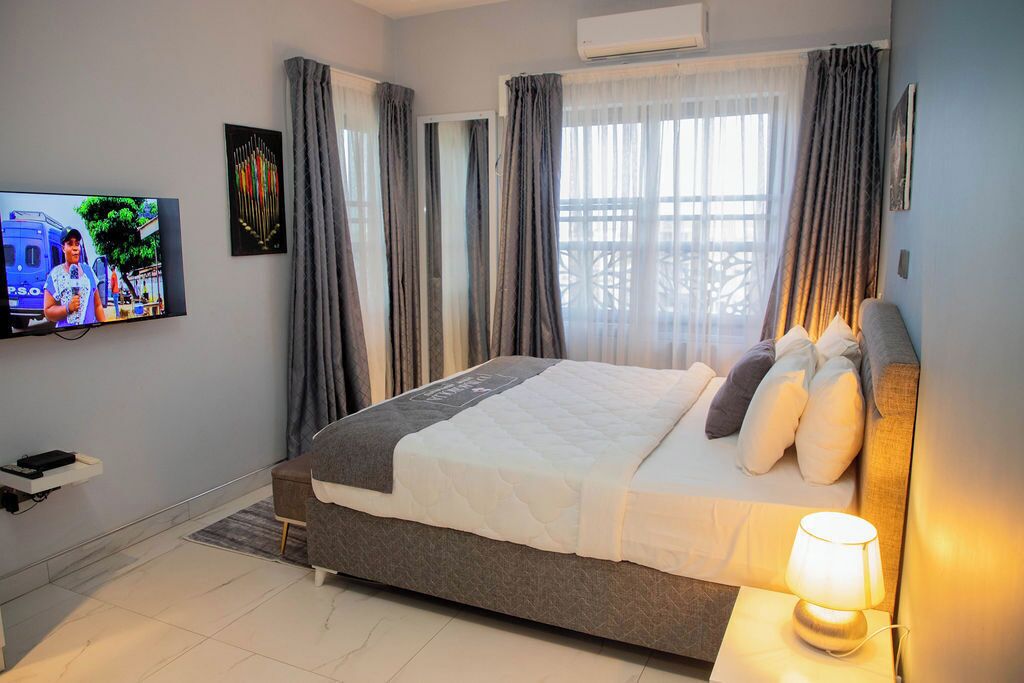 A bedroom with a bed, a TV, a bedside table with a lamp, and a window with curtains.