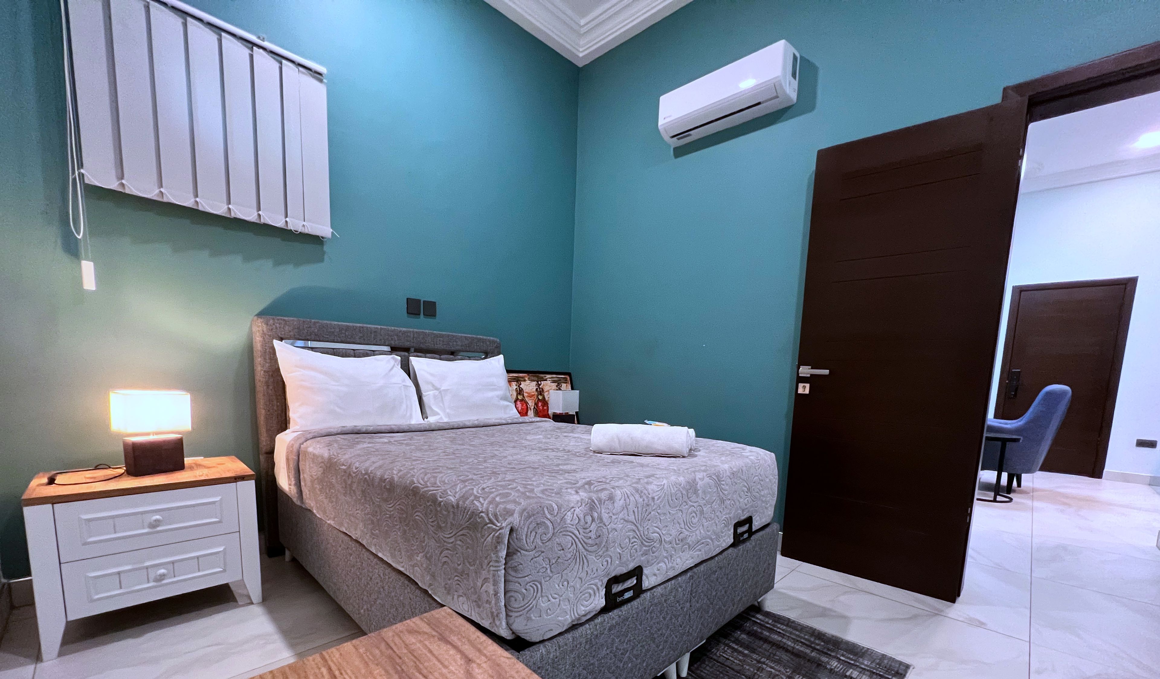Een slaapkamer met een bed, nachtkastje, lamp en een wandairconditioner.