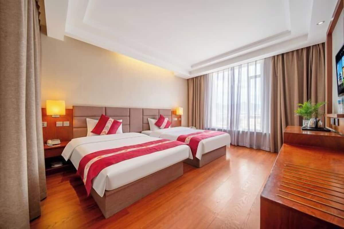 A hotel room with two beds, a wooden floor, a desk, and a television.