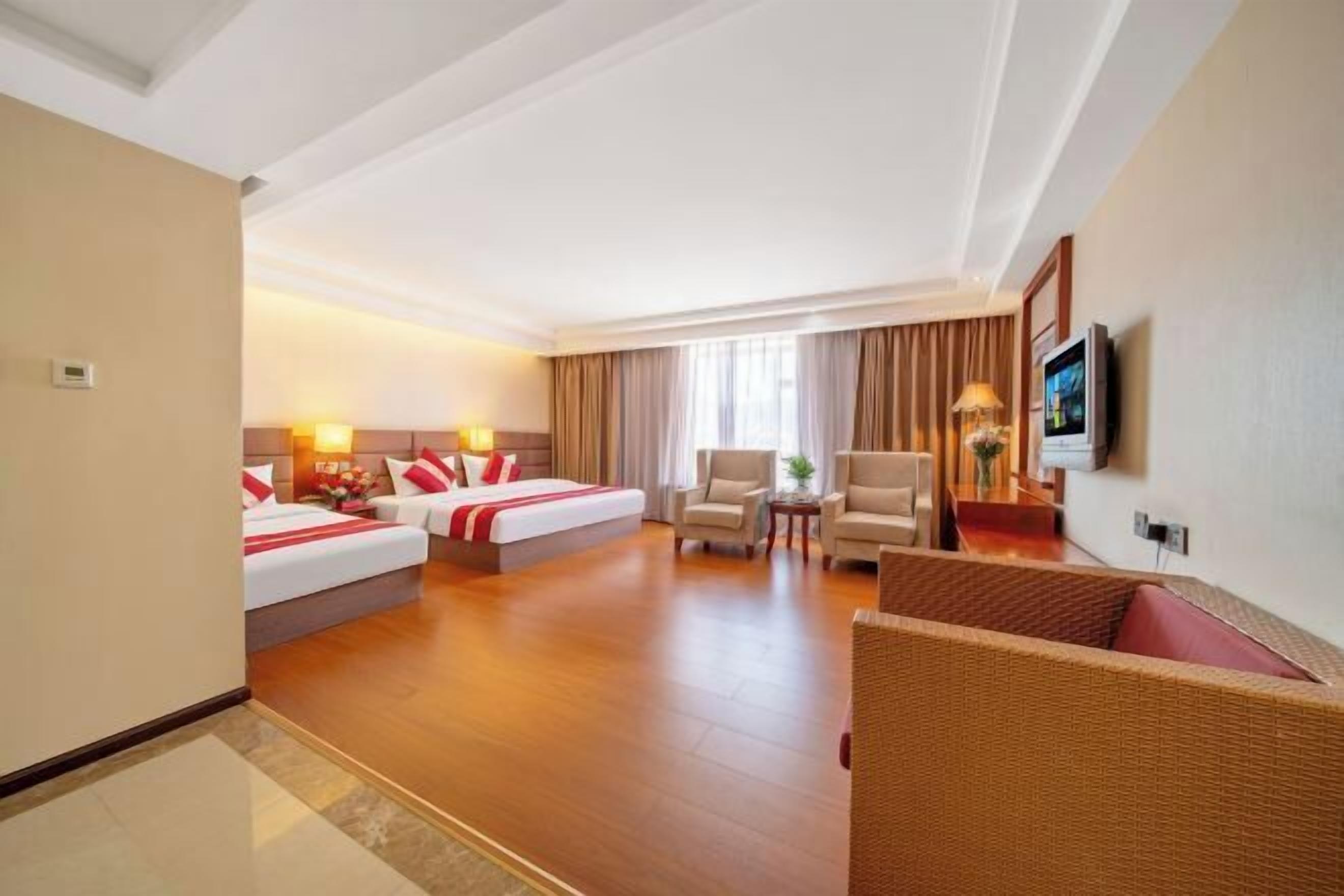 A hotel room with two beds, a sofa, a TV, and a window with curtains.